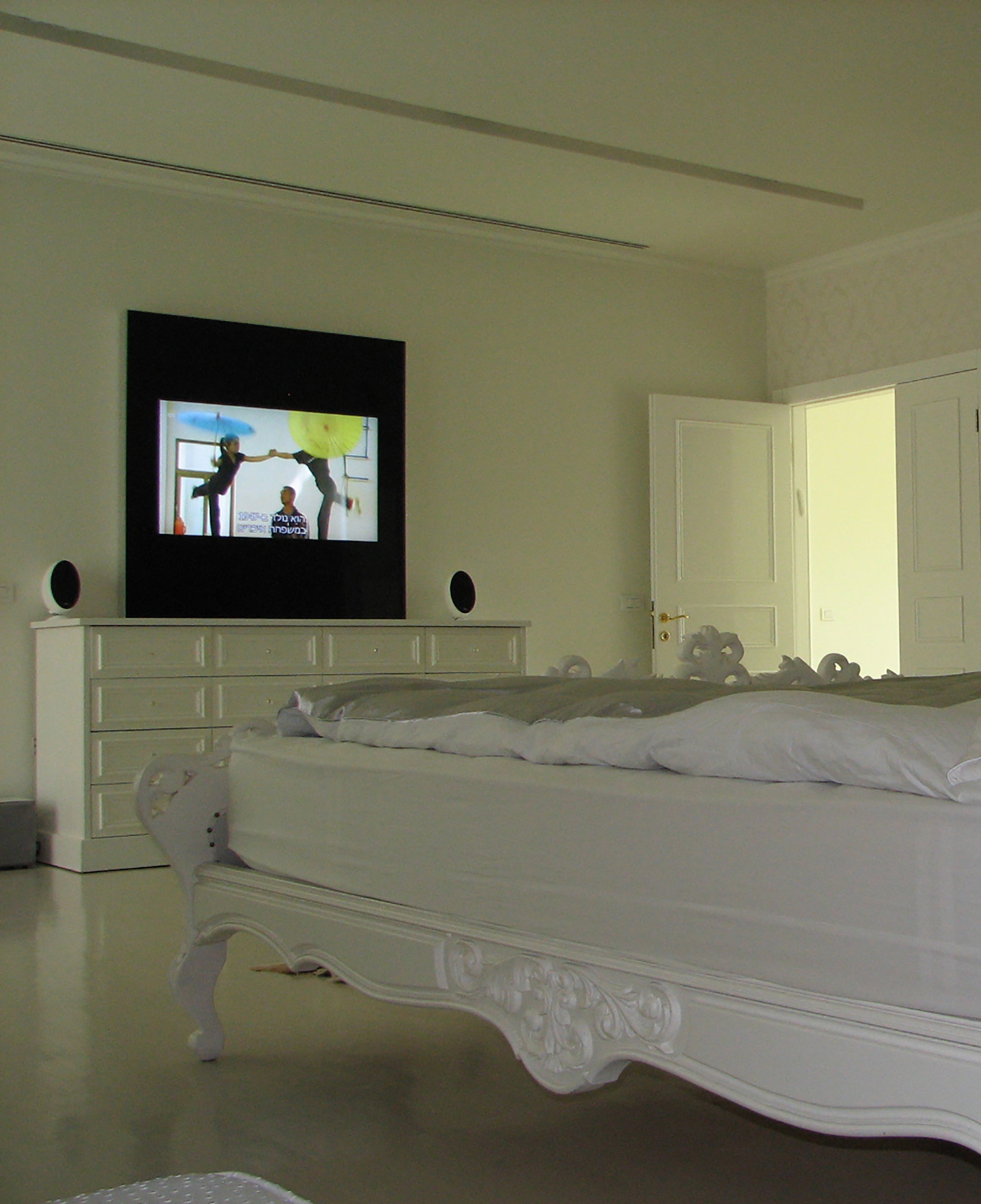 White bed with decorative headboard in a room with a television on a stand.