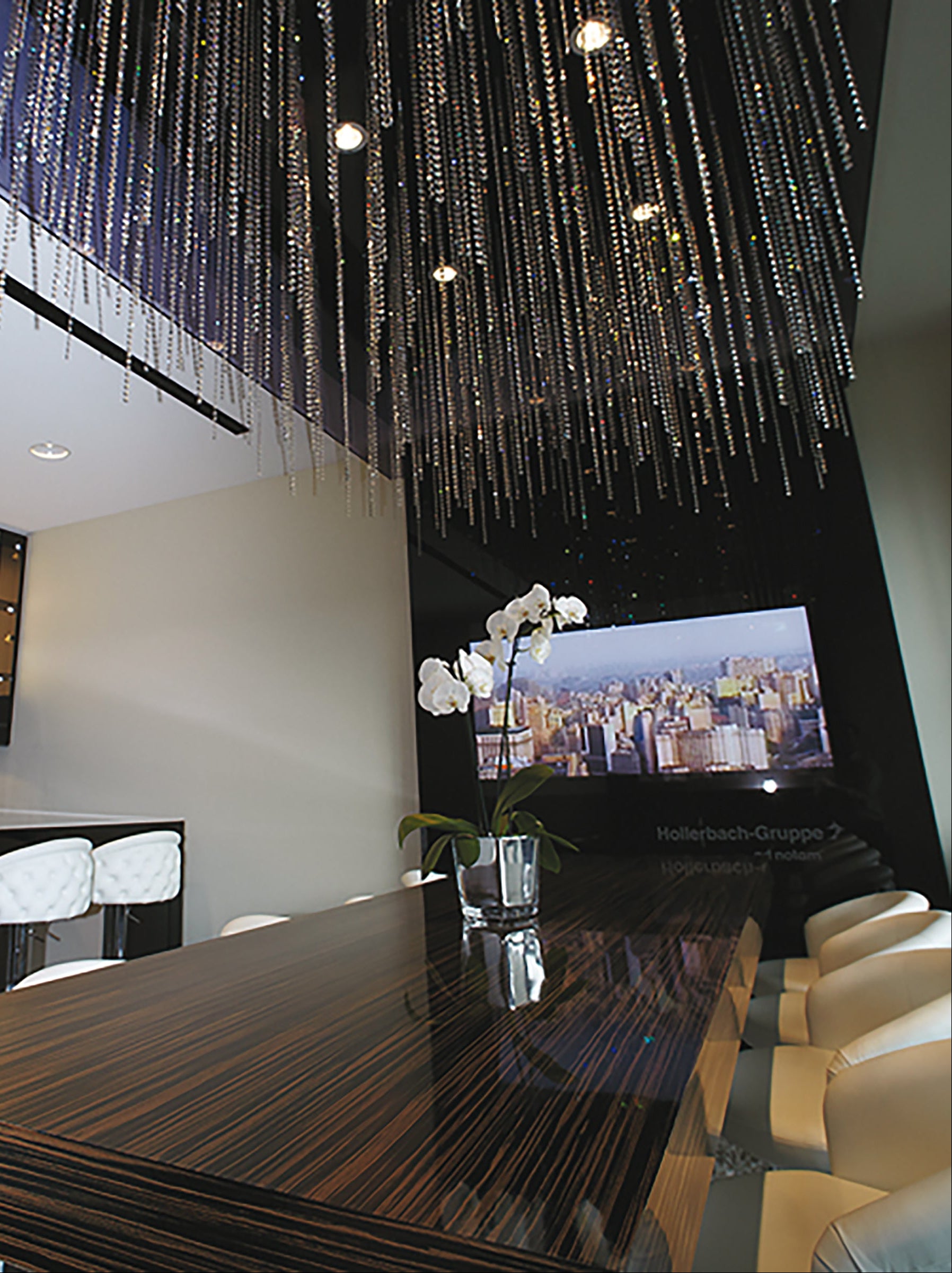 Modern dining room with a large chandelier, dark wooden table, and white chairs.